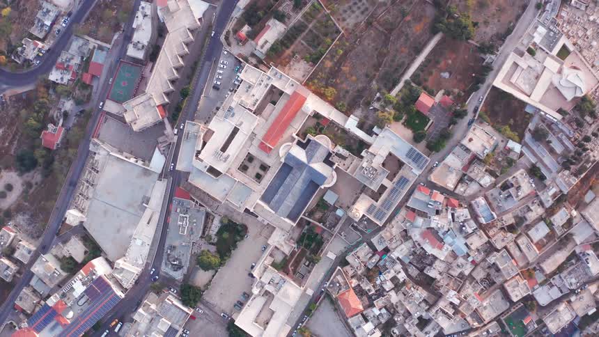 An ascending top-down aerial view reveals the Basilica of the Annunciation surrounded by the dense urban landscape of Nazareth, Israel