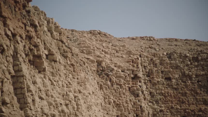 Slow pan across the weathered and crumbling mud brick walls of an ancient ruin in an arid, desert landscape