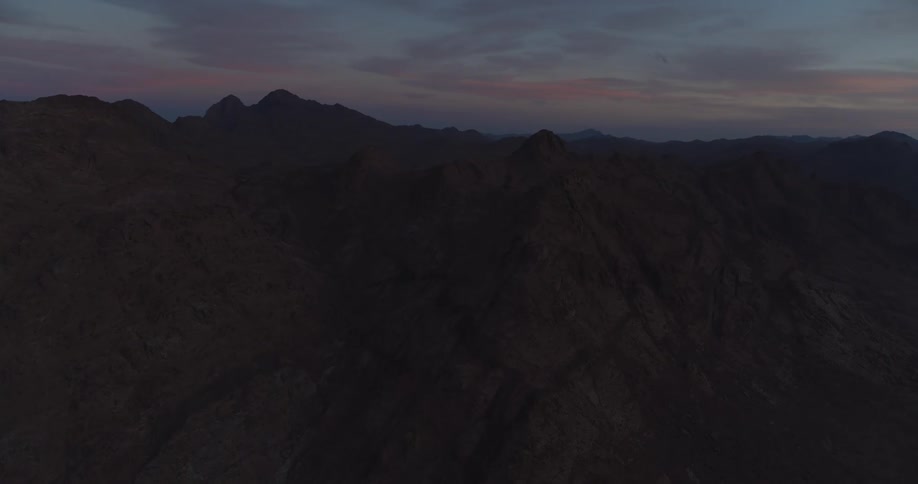 A wide, static shot shows a vast and desolate mountain range under a serene twilight sky