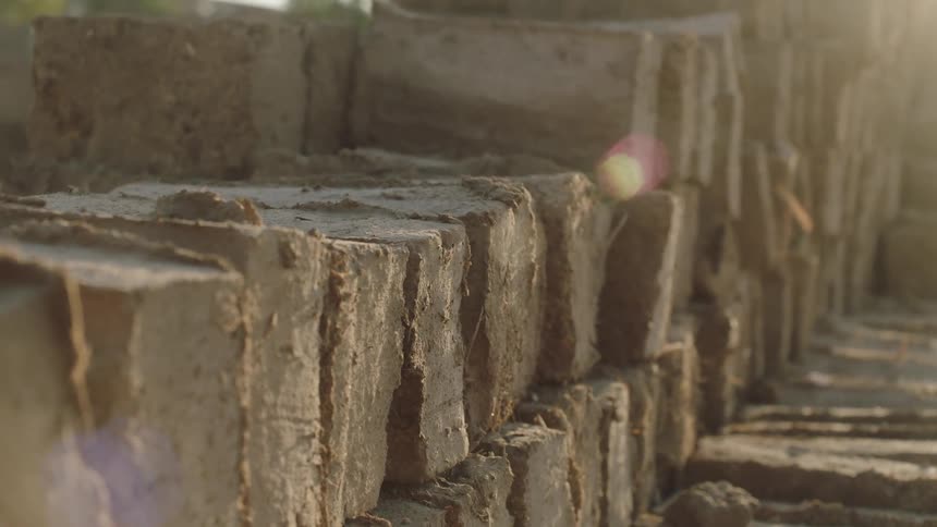 A close-up dolly shot of handmade mud bricks stacked in rows to dry in the warm sunlight