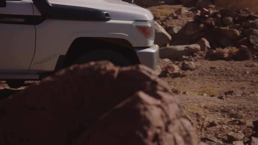 A slow pan shot of a white 4x4 vehicle driving over a rocky and arid desert terrain