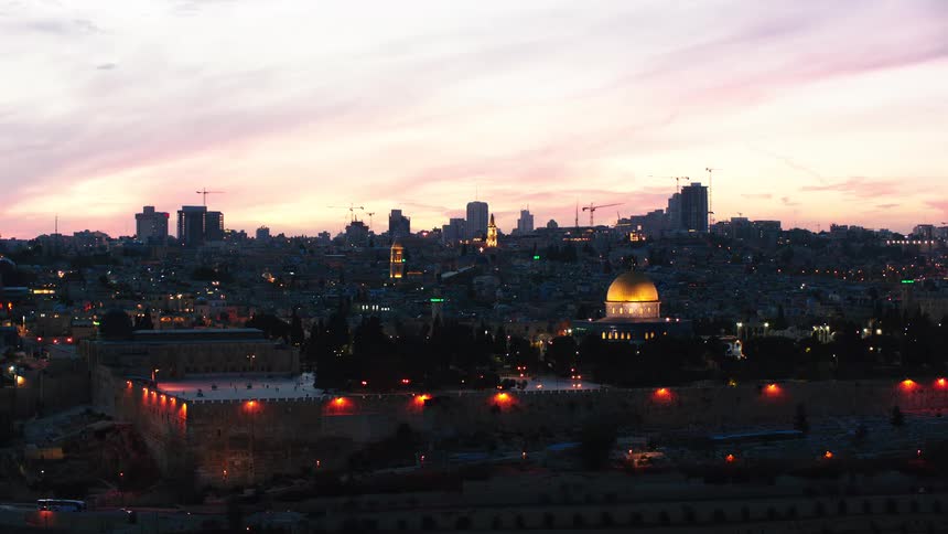 The illuminated Dome of the Rock and the Old City of Jerusalem are bathed in the soft light of a colorful sunset