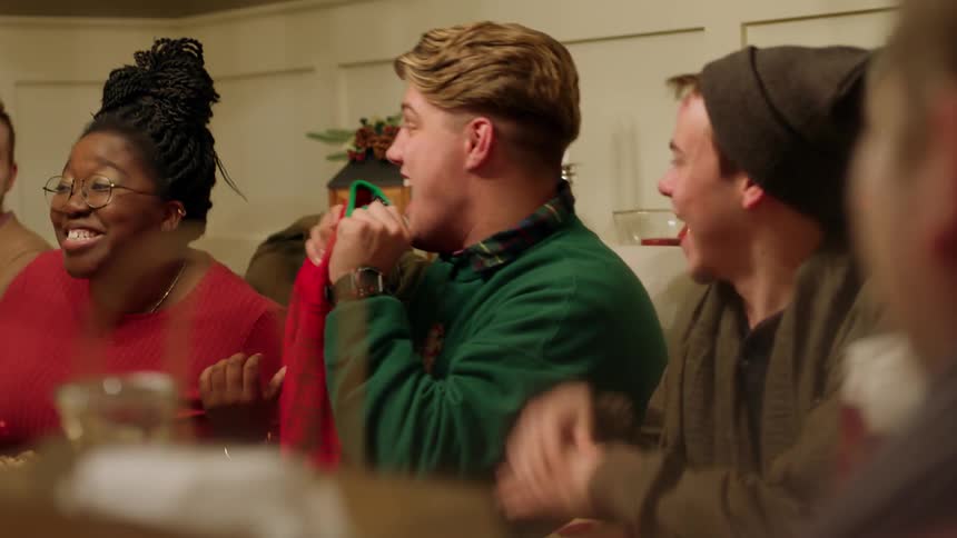 A man opens a gift and raises a sweater in front of friends