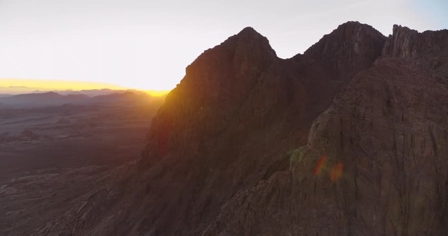 Cinematic drone footage reveals a glorious sunrise from behind a rugged mountain in the Sinai desert