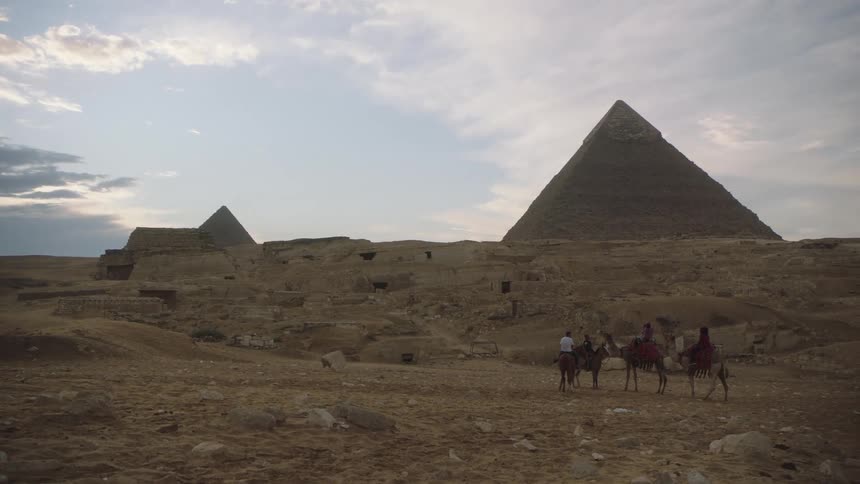 A camel caravan of tourists pauses to take in the majestic view of the Great Pyramids of Giza at dusk