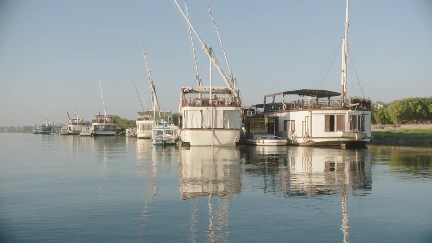 Traditional Egyptian felucca boats and Dahabiyas are moored peacefully along the banks of the Nile River