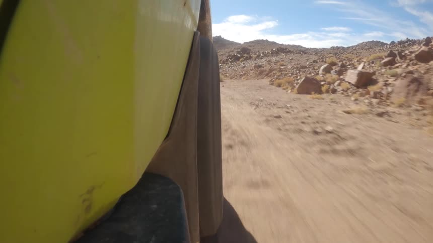 A point-of-view shot from a lime-green off-road vehicle as it drives along a bumpy, sandy trail through a rocky desert canyon