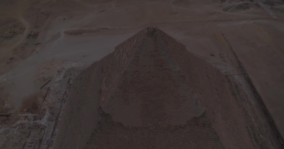 Majestic aerial view slowly pulls back from the top of an ancient Egyptian pyramid, revealing the iconic Giza Necropolis in the vast desert