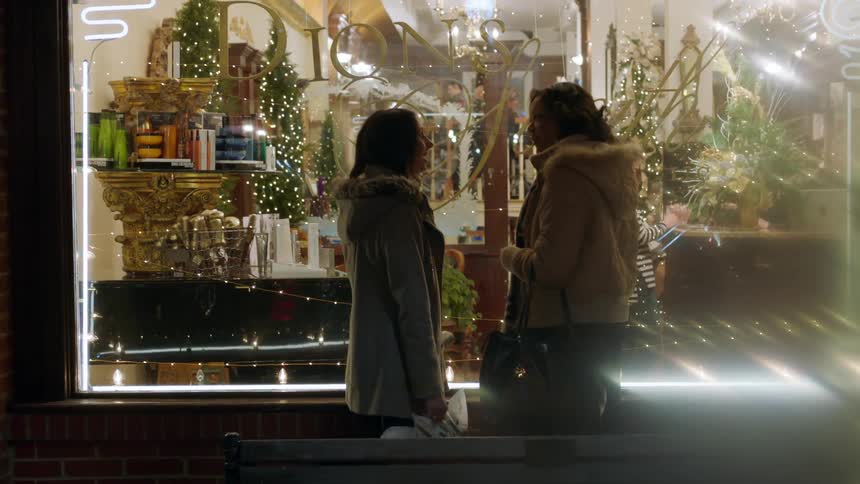 Two women talk as they stand in front of a shop window at night