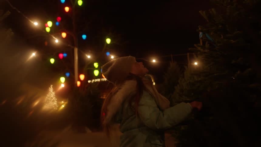 A girl looks at a tree on a christmas tree lot