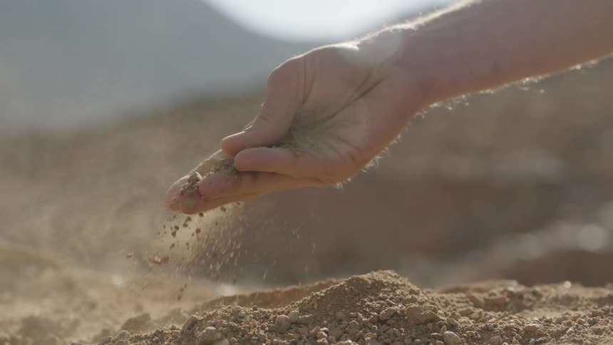 A close-up slow-motion shot of a hand letting dry earth and sand slip through its fingers back to the ground