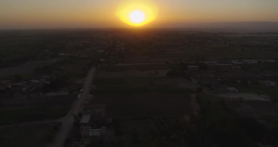 A stunning aerial view captures the golden sunset over a peaceful rural village and its surrounding farmlands