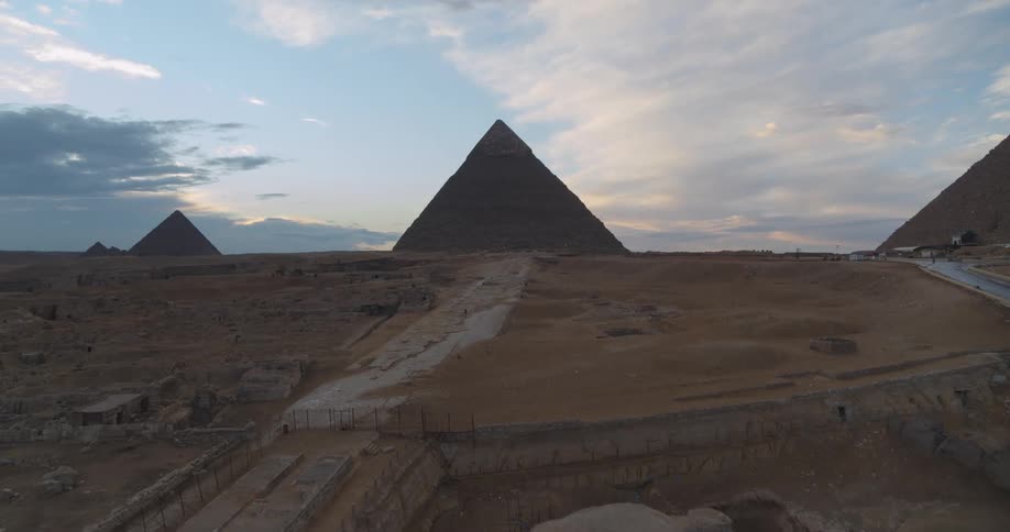 An aerial drone shot flies over the iconic Great Sphinx toward the majestic Pyramids of Giza at dusk