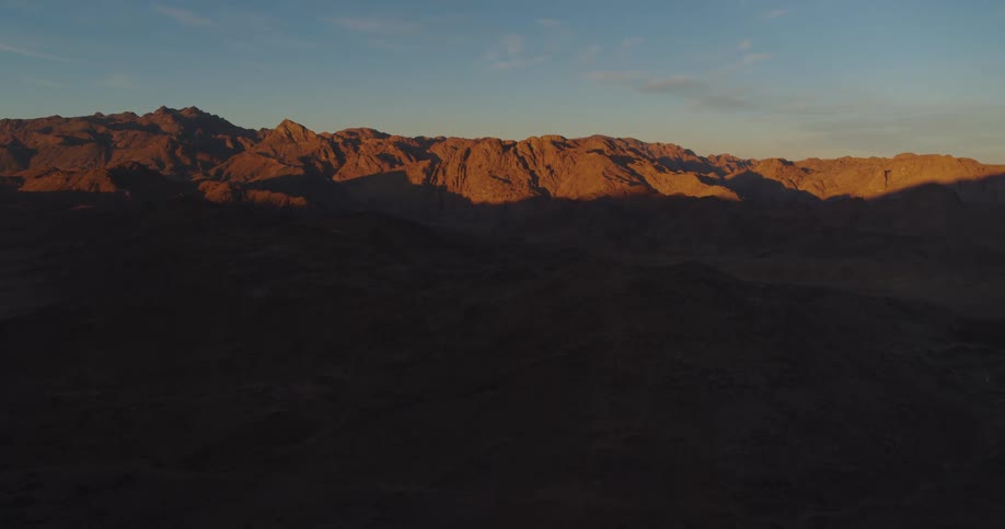 A majestic aerial shot captures the golden light of sunrise hitting the peaks of a vast desert mountain range