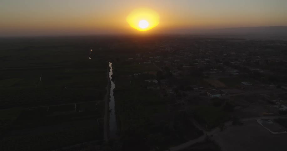Aerial view of a vibrant sunset over a rural landscape with a canal separating farmland from a small town