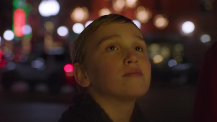 Child standing in the middle of a city at night looking up