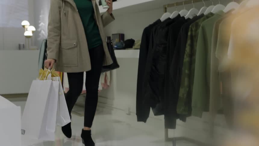 Woman carrying a shopping bag looks at a  rack of clothing