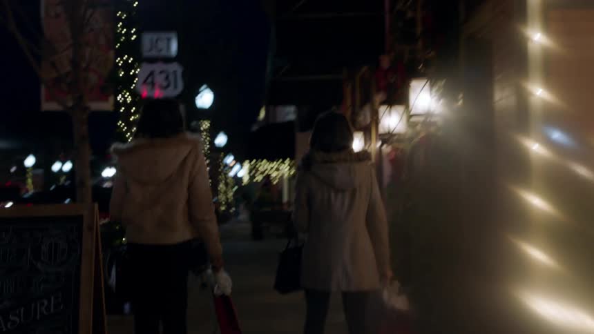 Two women walking in down a street with shops lit up for christmas