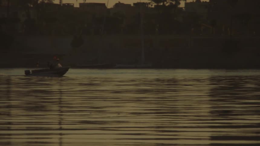 A small motorboat peacefully sails across the calm, golden river at sunset