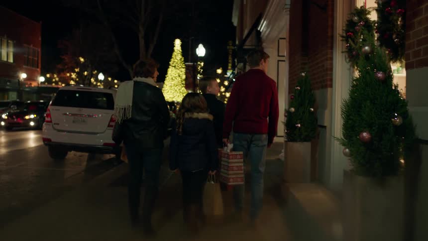 A family walks down a city sidewalk at christmastime