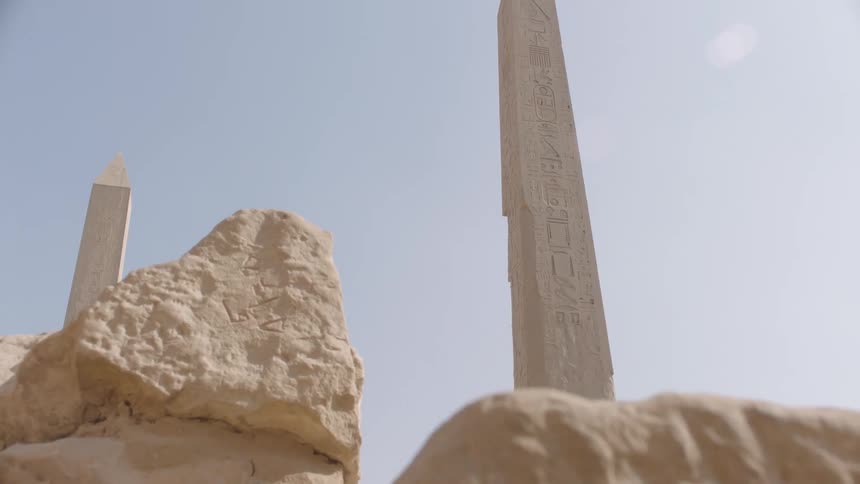 Gazing up at a magnificent ancient Egyptian obelisk covered in hieroglyphs from behind crumbling stone ruins