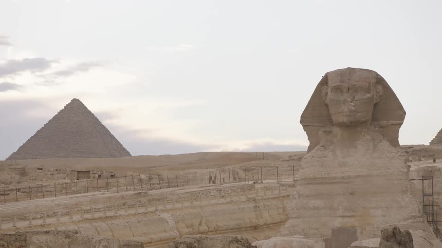 The majestic Great Sphinx of Giza stands proudly with the Khafre Pyramid in the background under a soft, overcast sky in the Egyptian desert