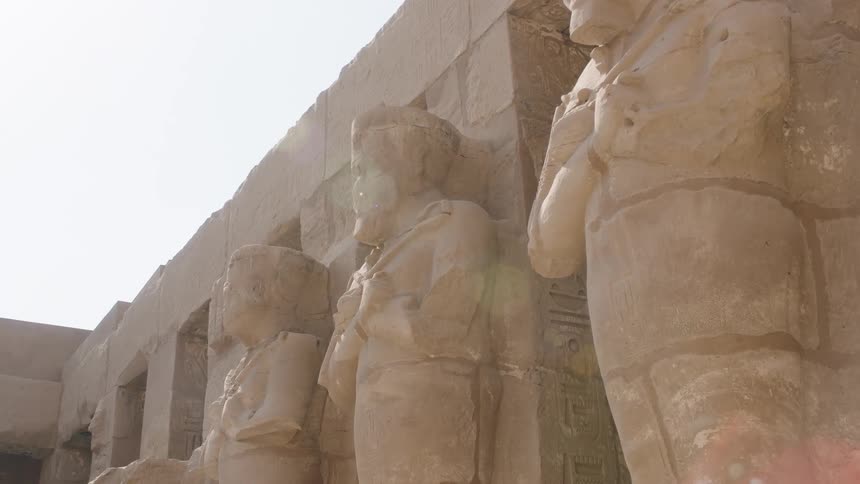 A low angle shot of ancient Egyptian statues carved into a temple wall under the bright desert sun