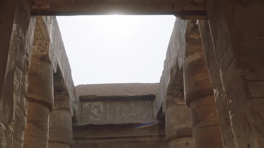 Sunlight streams through the open roof of an ancient Egyptian temple, illuminating massive stone columns with carved hieroglyphics