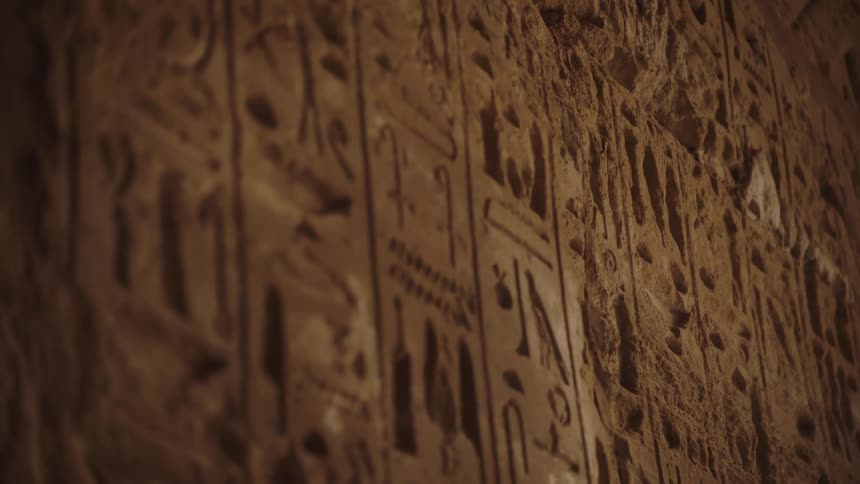 A close-up rack focus shot reveals ancient Egyptian hieroglyphics carved into a stone temple wall