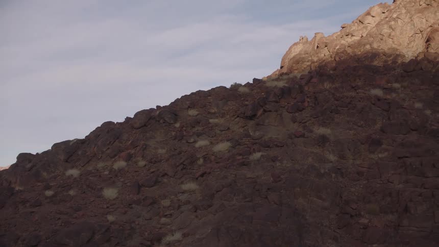 Morning light illuminates the peak of a rugged, rocky mountain as the camera slowly tilts upwards