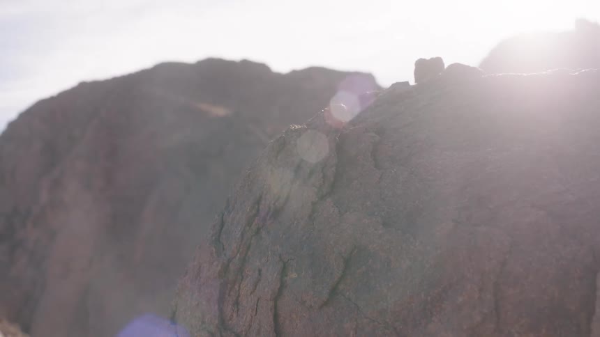 A man's hand reaches out and gently touches a sunlit boulder in a rocky desert landscape