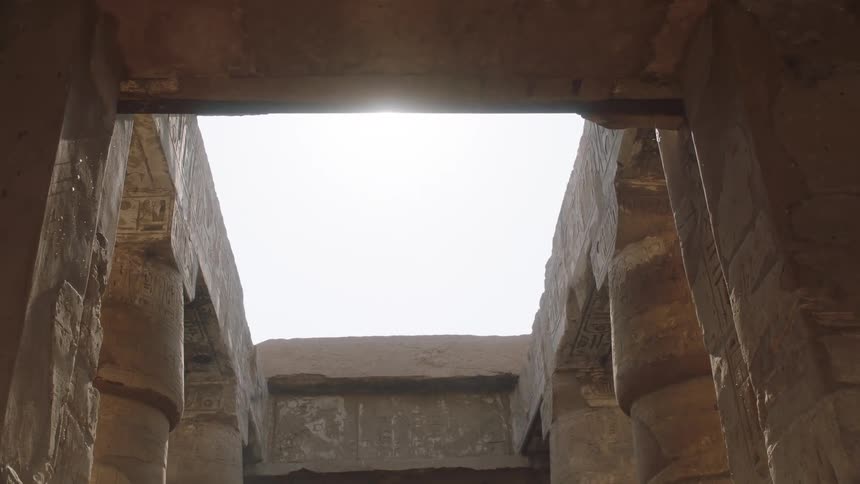 The bright sun flares as it shines through an opening in the roof of an ancient Egyptian temple with hieroglyphics