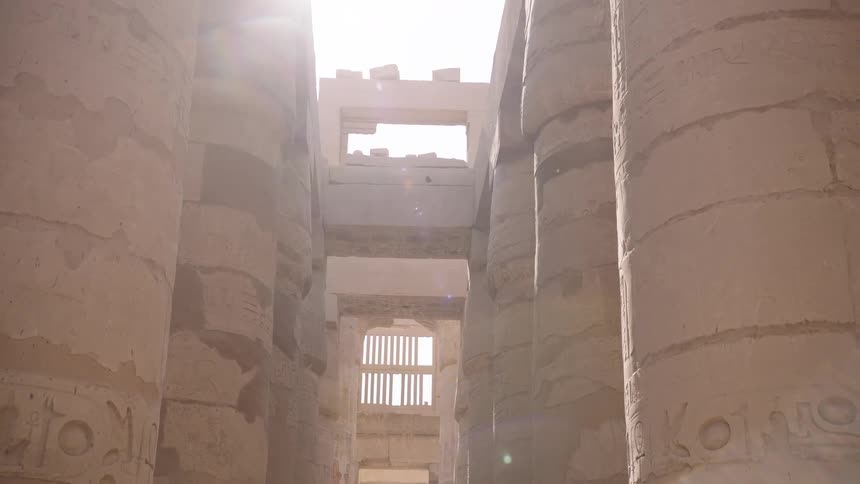 A bright sun flare illuminates the massive, carved stone columns inside an ancient Egyptian temple