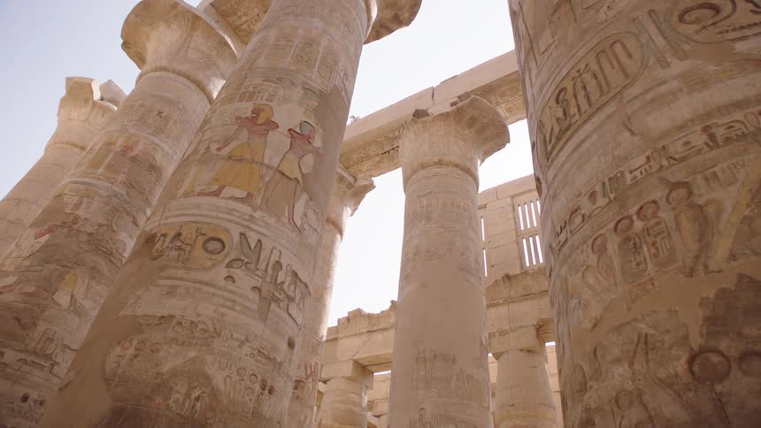 A low-angle view of the massive, intricately carved columns with faded paint and hieroglyphics inside an ancient Egyptian temple