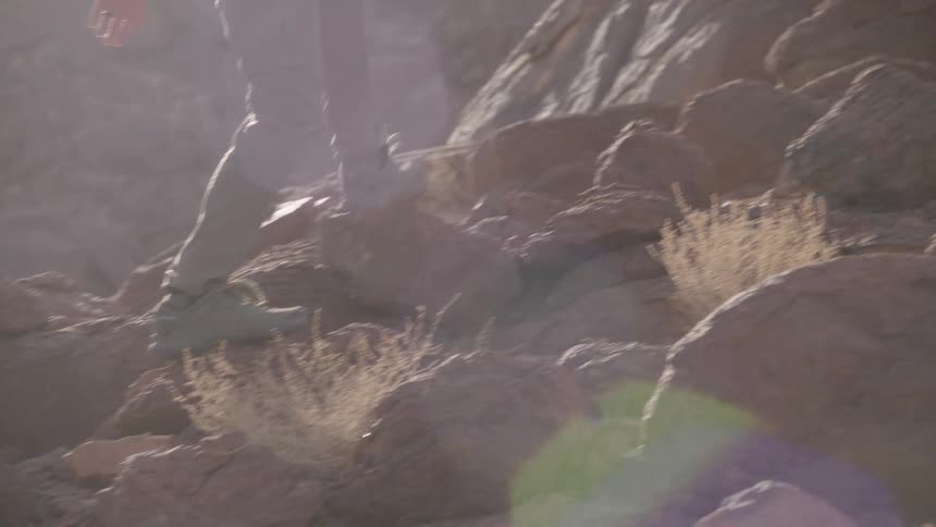 Close-up slow motion shot of a hiker's feet in boots walking and climbing up a rocky, sunlit mountain trail