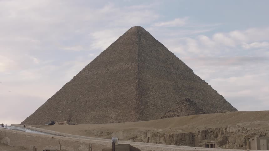 A wide, static shot of the Great Pyramid of Giza standing majestically in the desert under a partly cloudy sky