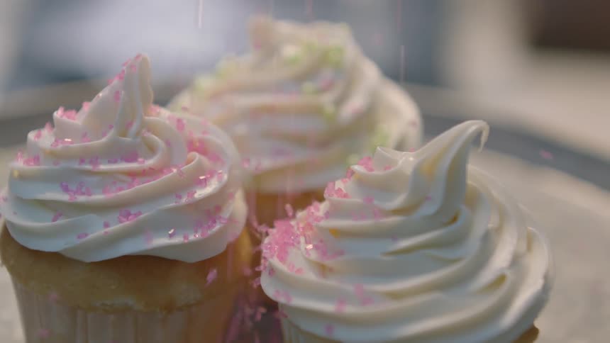 A person drops sprinkles on three cupcakes
