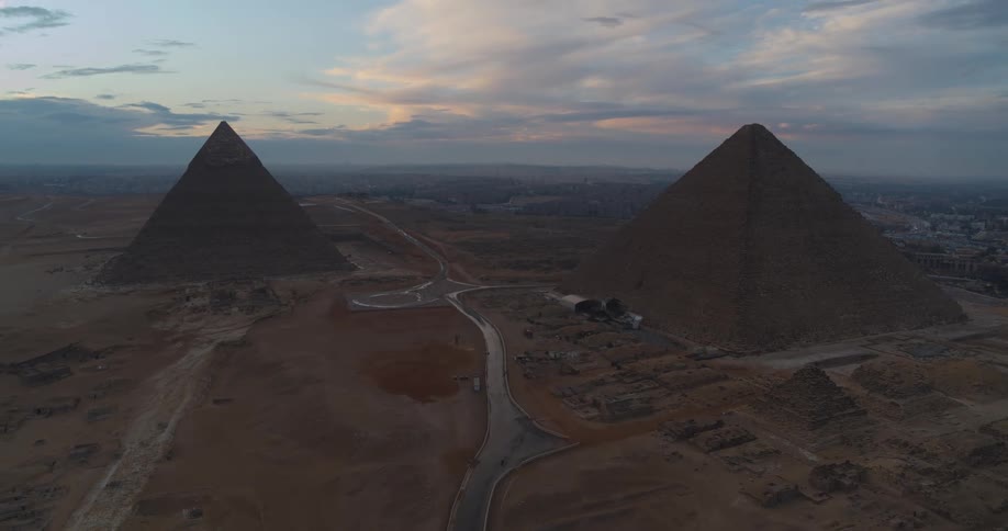 A slow aerial pullback reveals the majestic Pyramids of Giza at sunrise, with the ancient desert landscape and the city of Cairo in the background
