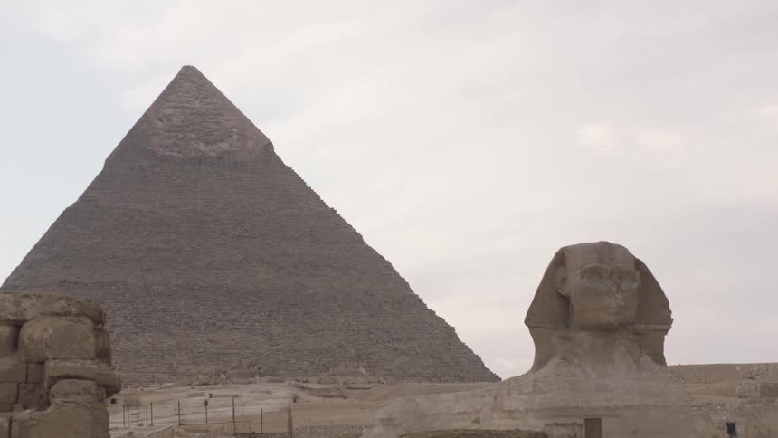 A slow zoom out reveals the iconic Great Sphinx with the Pyramid of Khafre looming in the background under a hazy sky in Giza, Egypt