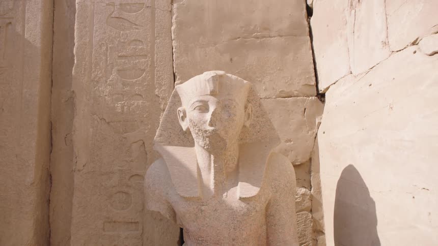A time-lapse of sunlight and shadows passing over a weathered ancient Egyptian pharaoh statue with hieroglyphics in the background
