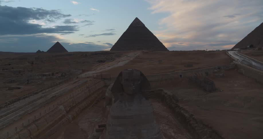 An awe-inspiring aerial flyover of the Great Sphinx of Giza, revealing the iconic pyramids in the background during a beautiful desert dusk