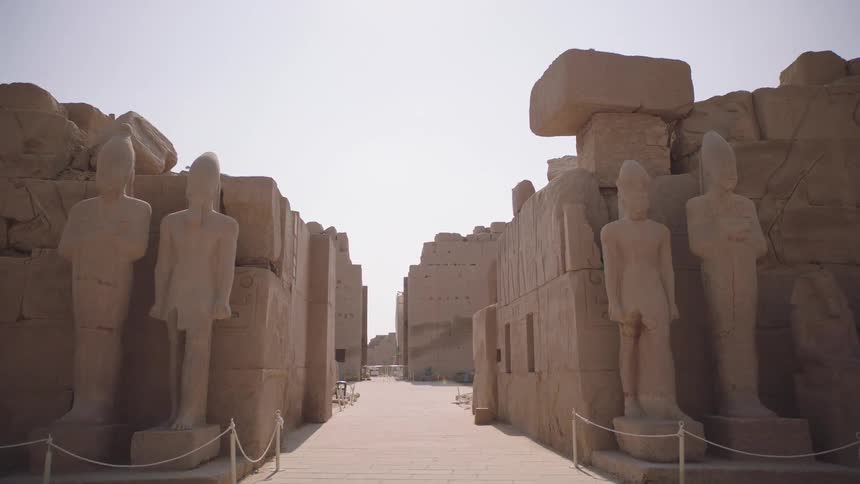 A slow reverse dolly shot reveals the grand walkway lined with towering pharaoh statues at the ancient Karnak Temple in Luxor, Egypt