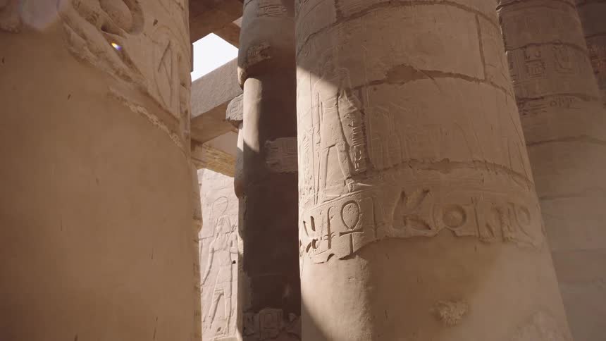 Sunlight casts shadows across massive stone pillars covered in ancient Egyptian hieroglyphics inside the Karnak Temple