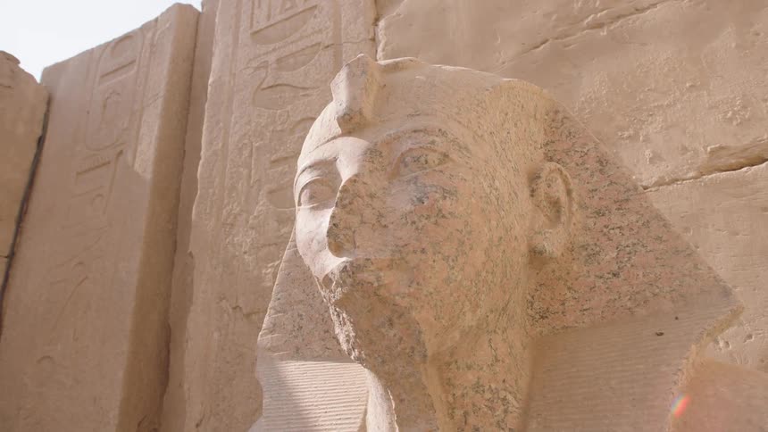 Slow upward pan reveals the majestic stone face of a pharaoh statue in an ancient Egyptian temple