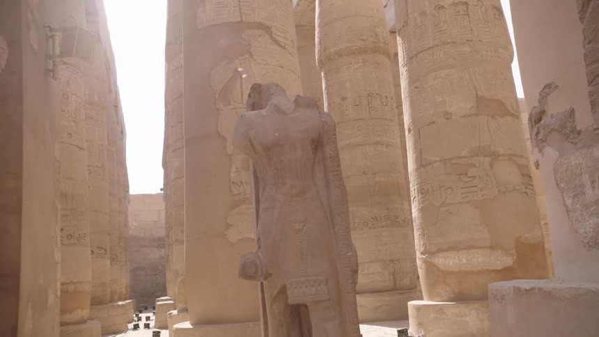 A slow pan reveals a headless pharaoh statue surrounded by ancient hieroglyphic columns at the Karnak Temple in Luxor, Egypt