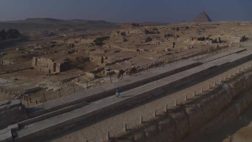 Aerial footage pans from behind the Great Sphinx to reveal the Giza pyramid complex, with tourists on camels in the foreground
