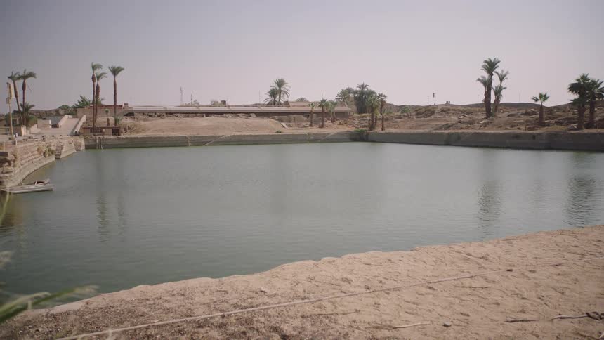 A tranquil man-made oasis with a large pool of water is revealed in an arid desert landscape