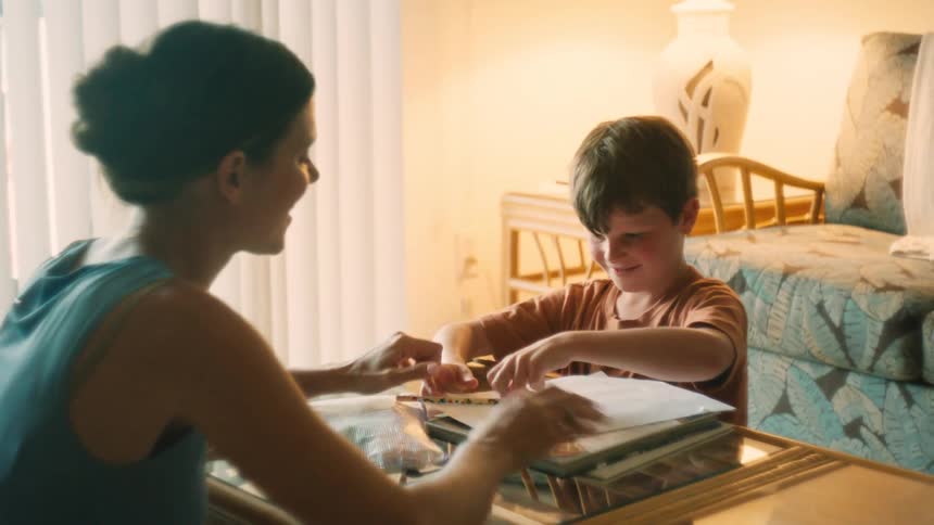 A loving mother encourages her young son with a high-five as he works on his homework at the living room table