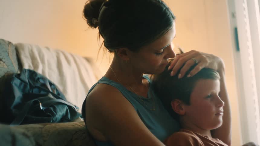 A tender moment between a mother and her son as she holds him close and kisses his head by a sunlit window