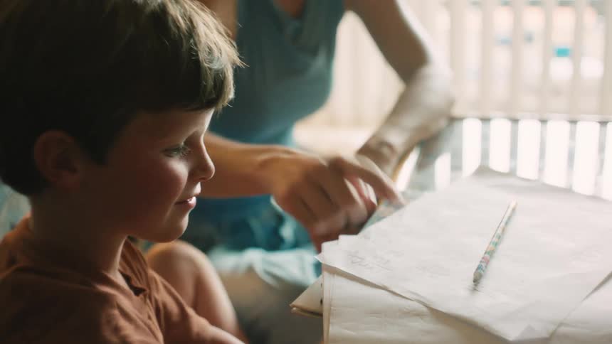 A young boy completes his homework with the help of his mother, and they celebrate with a happy high-five